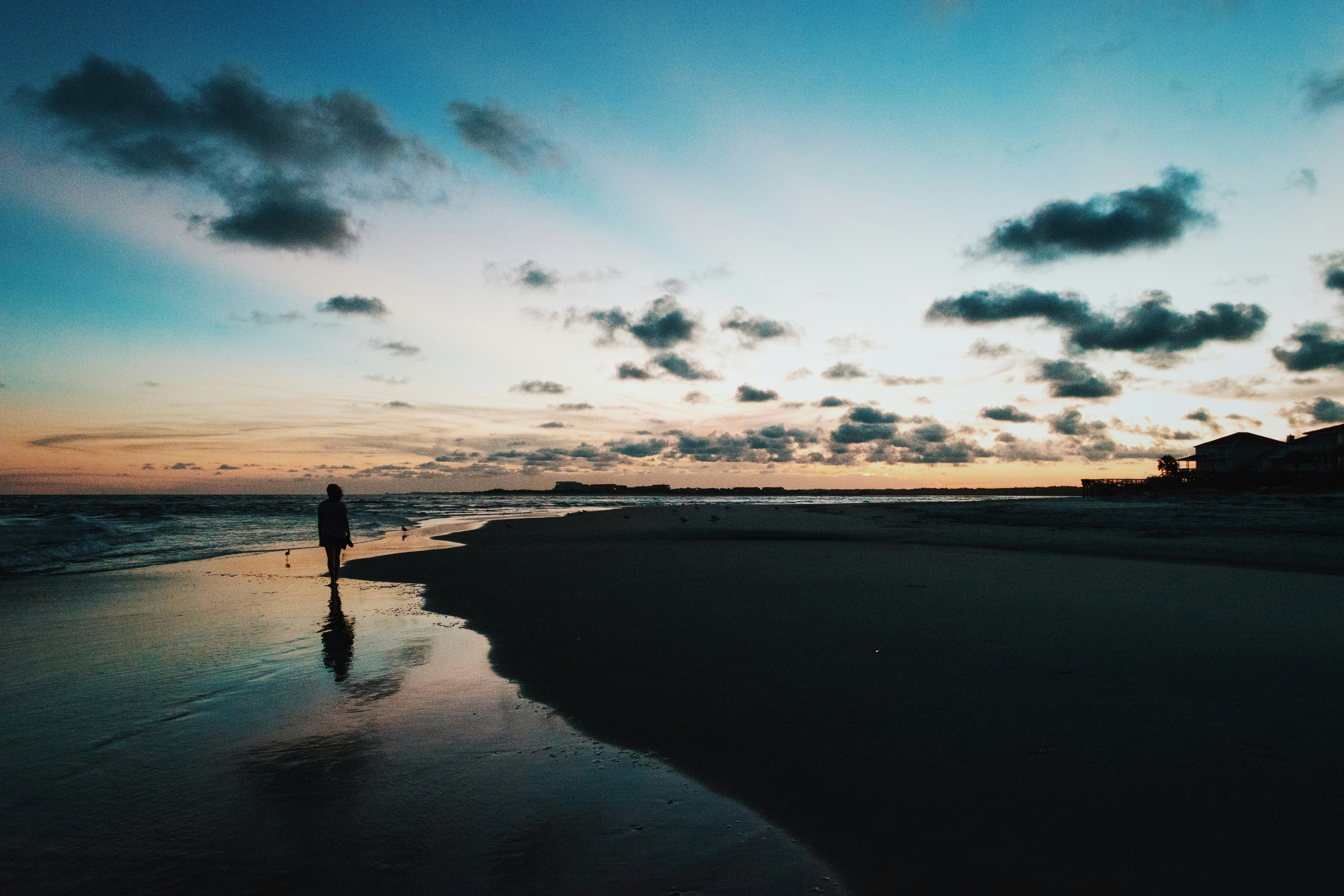 silhouette of person walk through beside ocean under blue and cloudy sky during sunset